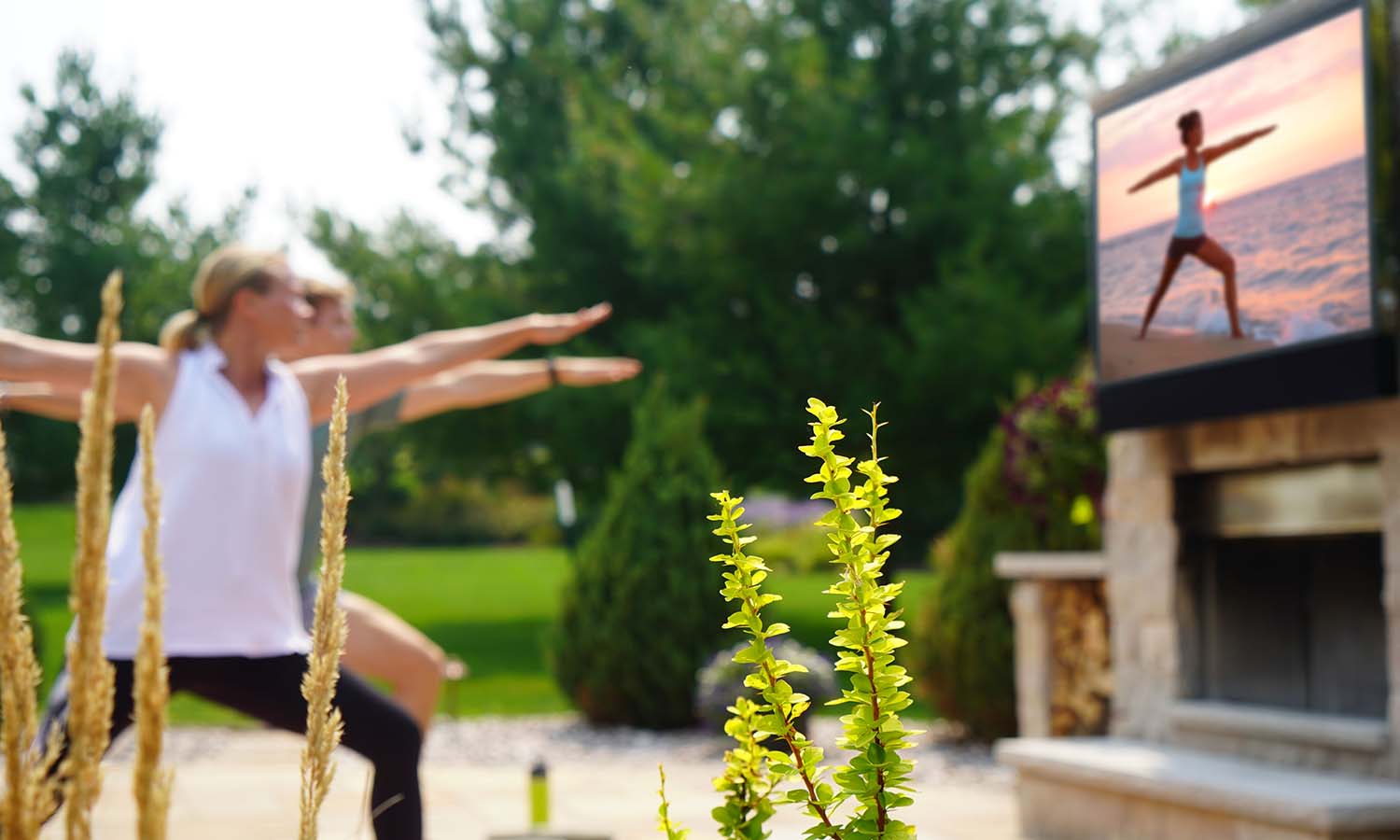 a couple perform yoga poses in front of an outdoor TV