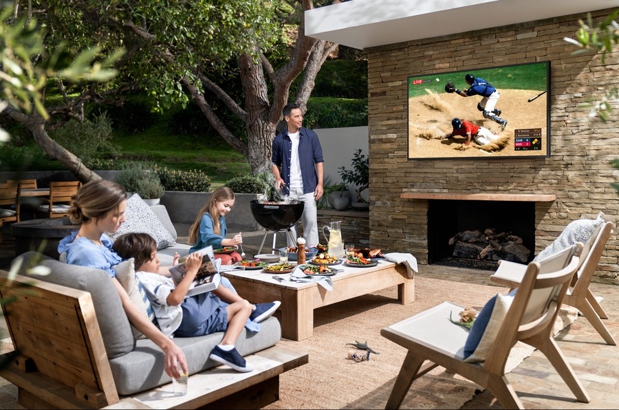 A family watching a baseball game on a Terrace Samsung Outdoor TV, while having a cookout.