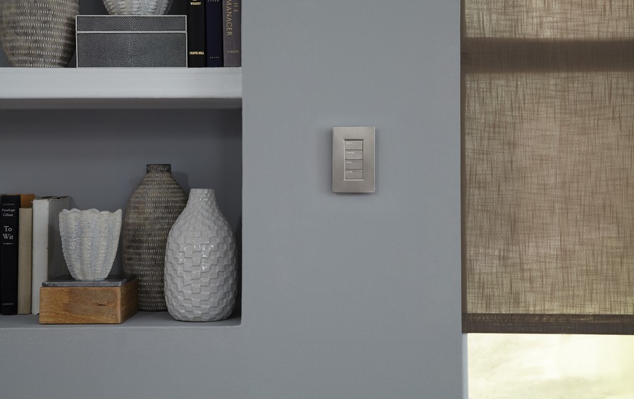 An elegant Lutron keypad on a wall next to motorized shades.