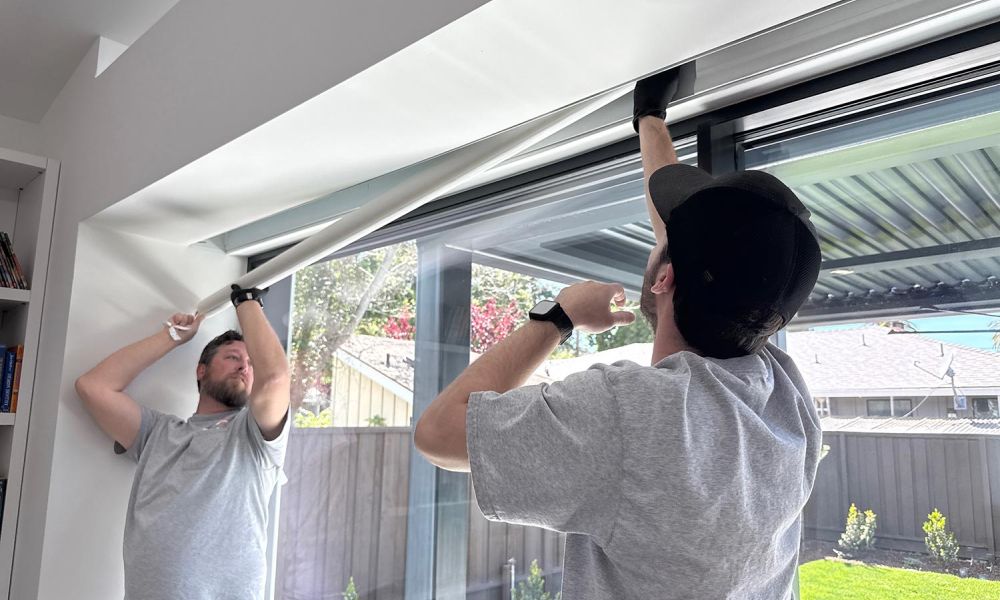 Two technicians installing a large white roller shade on a modern glass wall