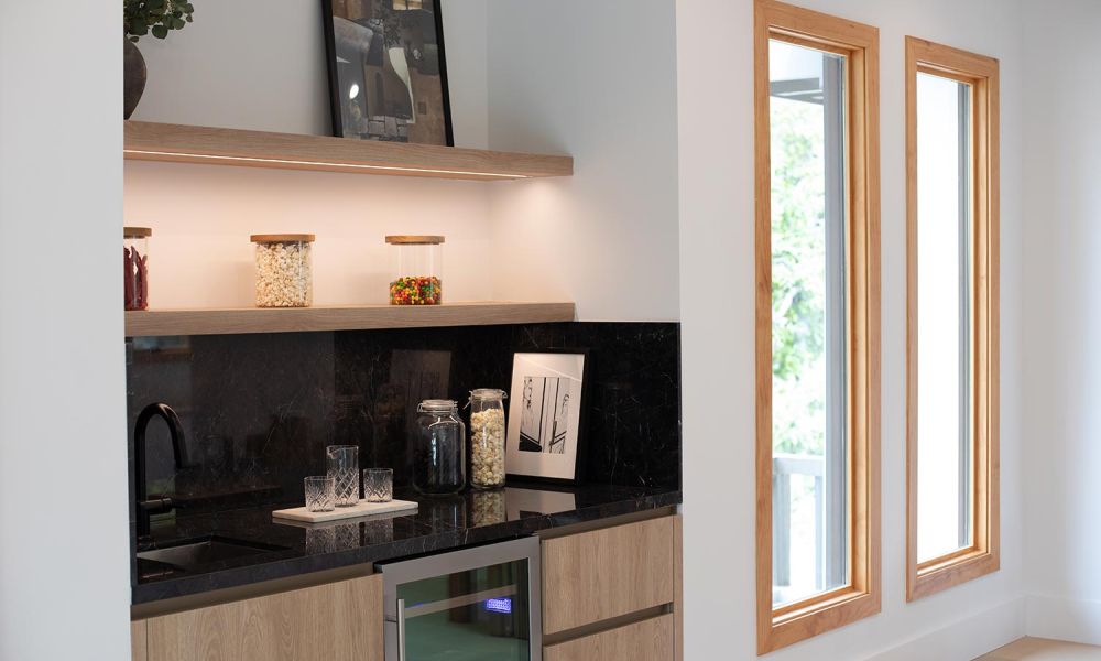 Mini bar setup with black marble counters, light wood shelving, and jars of snacks under soft LED shelf lighting