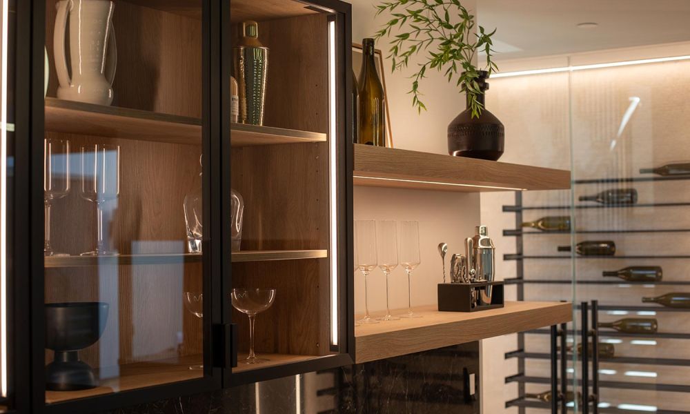 Angled view of a stylish bar with LED-lit shelves, glass cabinets, and a glass-enclosed wine display
