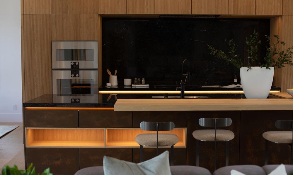 Sleek kitchen with black marble backsplash, light wood cabinetry, and integrated under-cabinet lighting