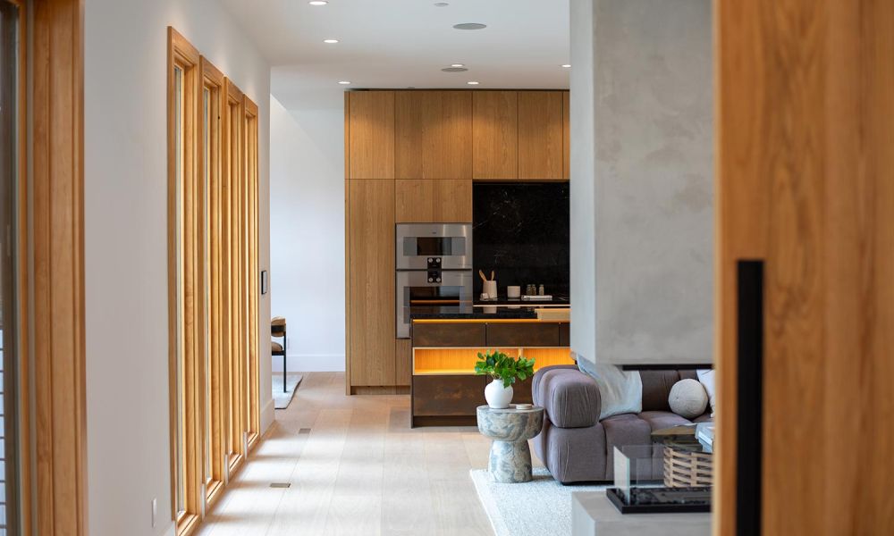 Long hallway view leading to a sleek kitchen with light wood finishes and under-shelf LED lighting