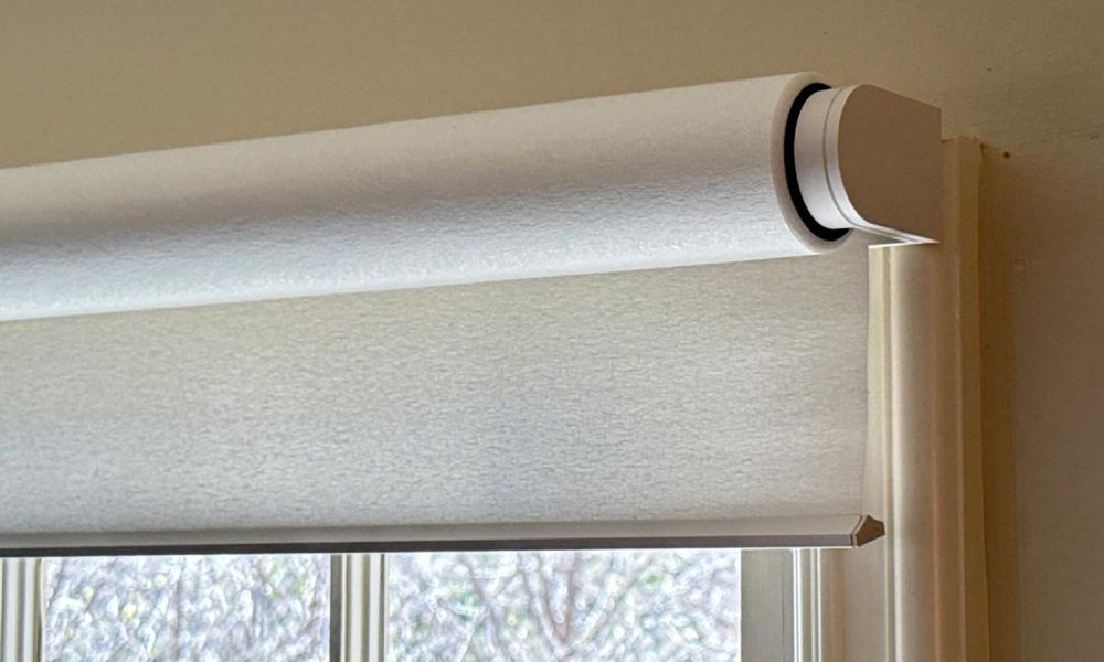 Detailed corner view of a white roller shade with minimal end cap mounted on cream-colored trim