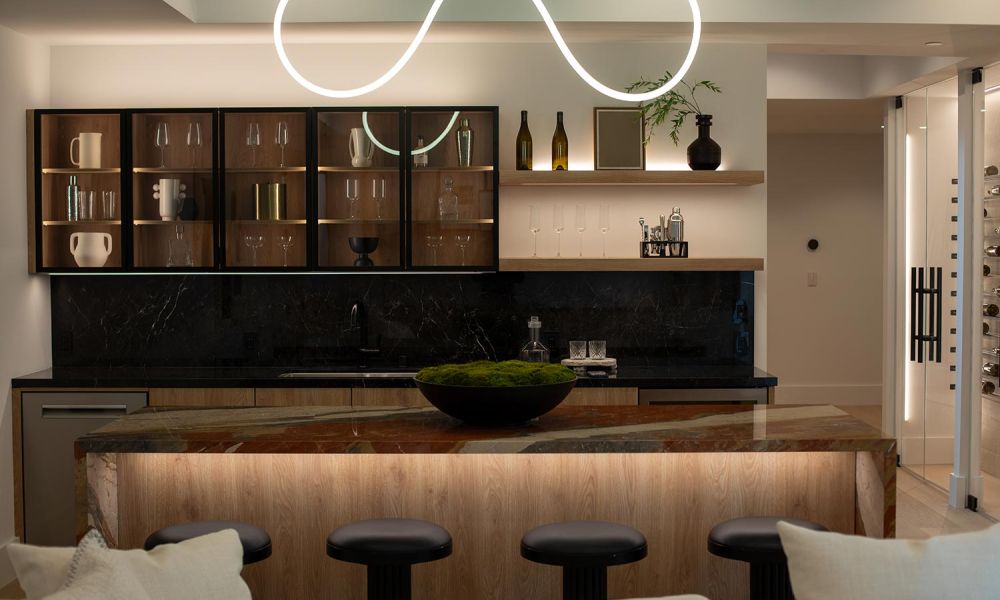 Full view of a modern bar with LED accent lighting, floating shelves, and curved pendant light above island