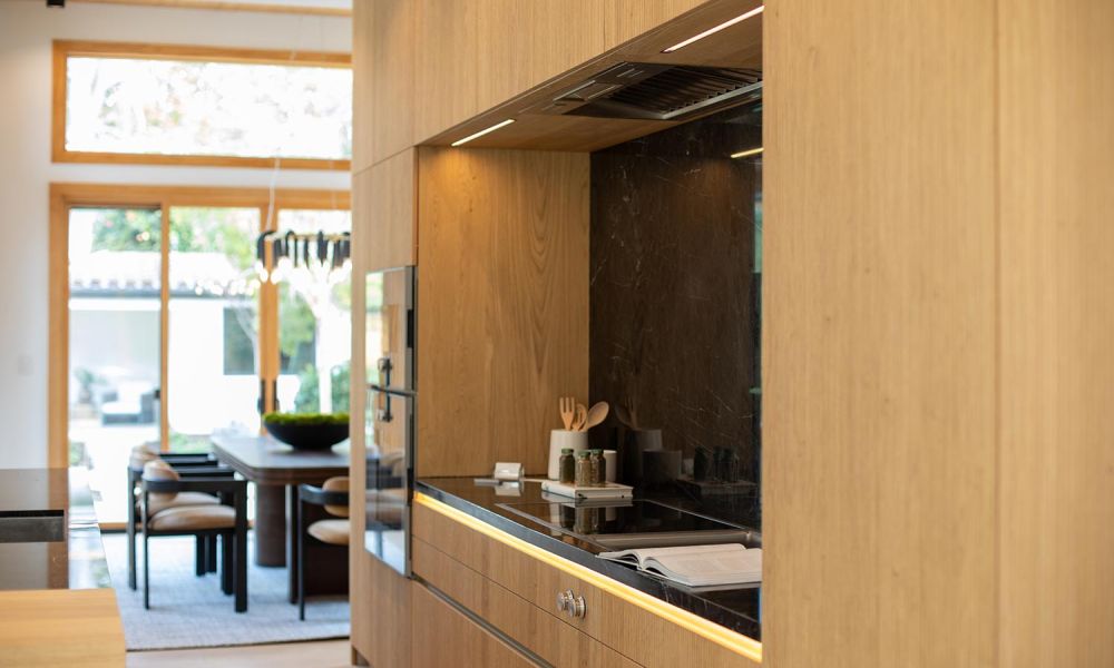 Kitchen with light wood cabinetry, black marble backsplash, and under-cabinet LED lighting near a dining area