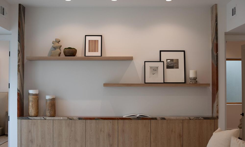Wall-mounted wooden shelves with framed art and sculptural décor in a softly lit living space