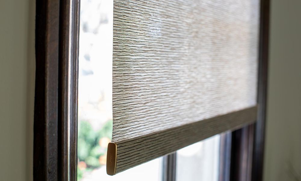 Lower edge of a roller shade with textured fabric hanging in front of a window