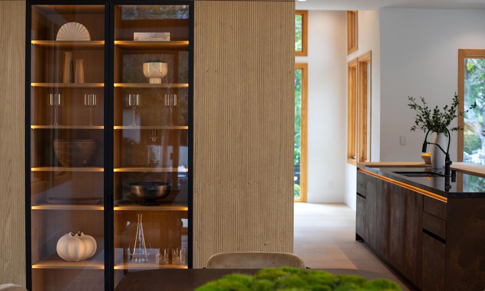 Illuminated display cabinet with wood shelves holding glassware and decorative items in a dining room