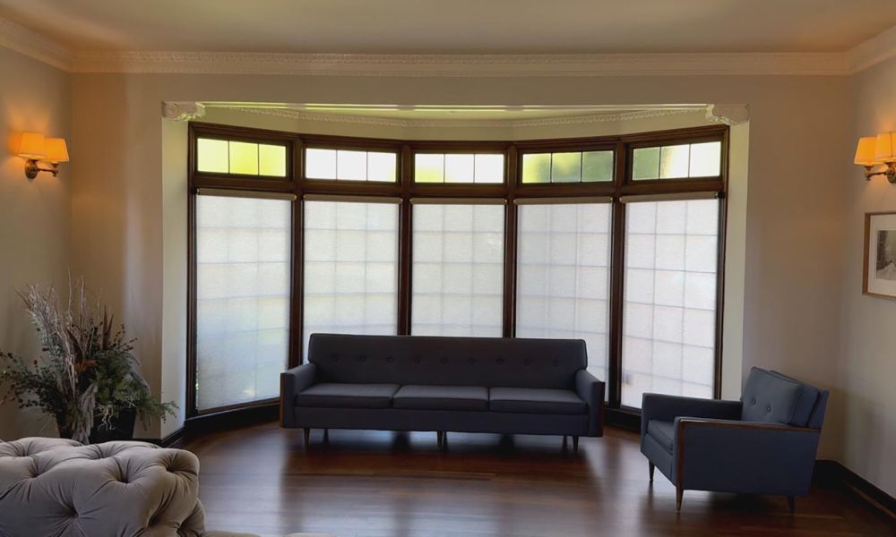 Living room with curved bay windows fitted with sheer roller shades and mid-century modern seating