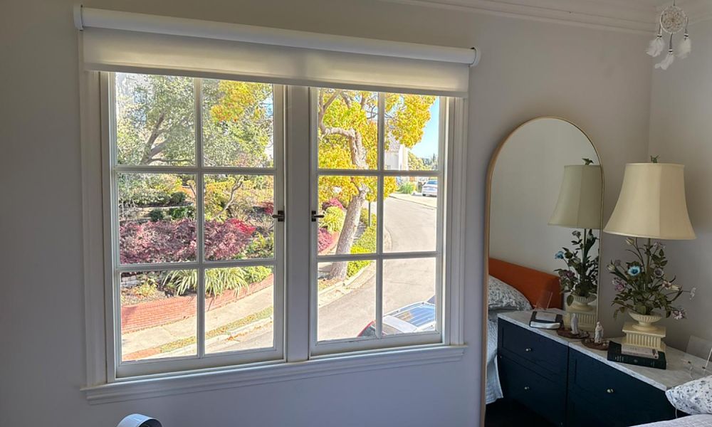 Bright bedroom with a white roller shade above a window showing a leafy neighborhood street